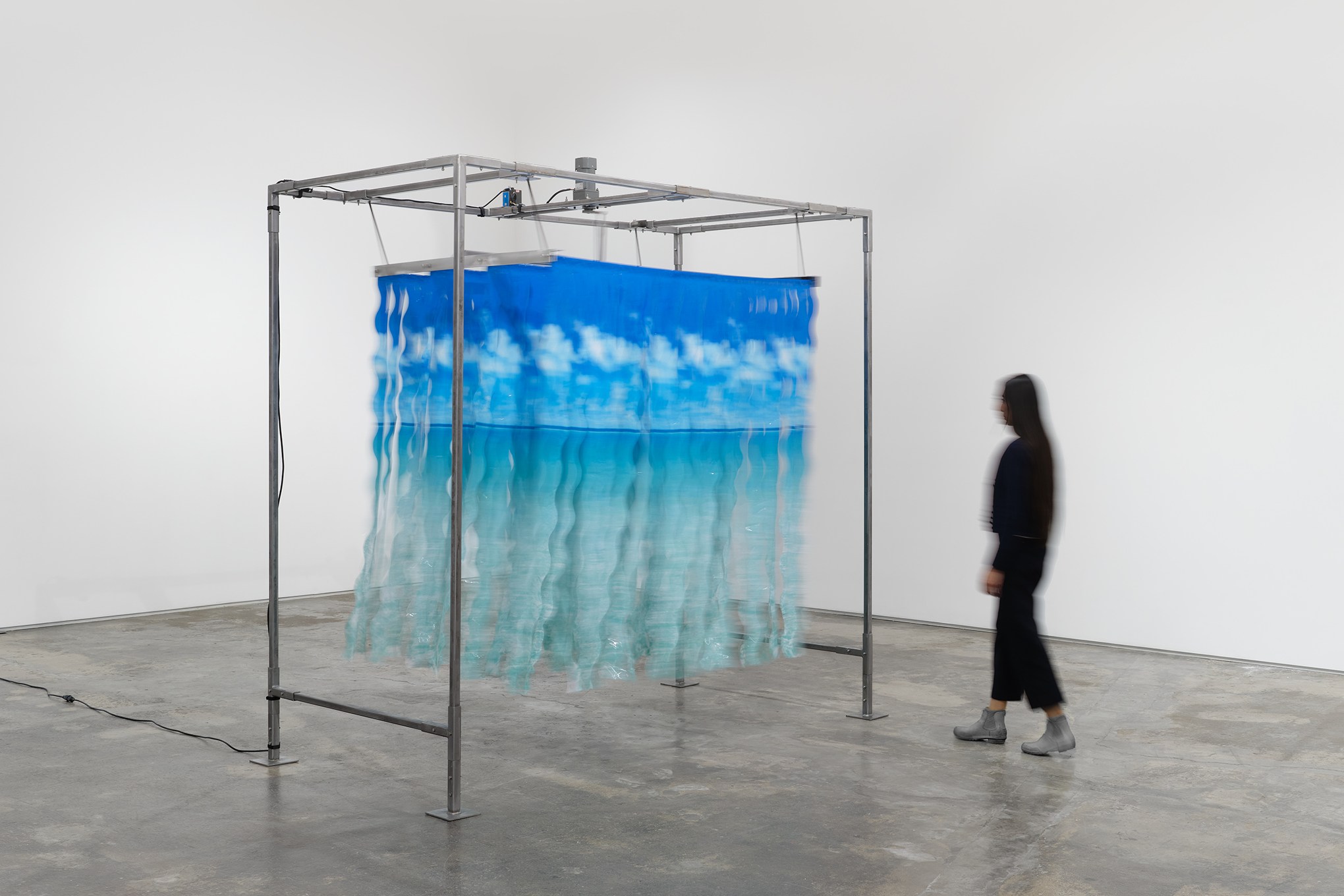 A shredded shower curtain depicting a beach scene hangs from a metal frame in the gallery.