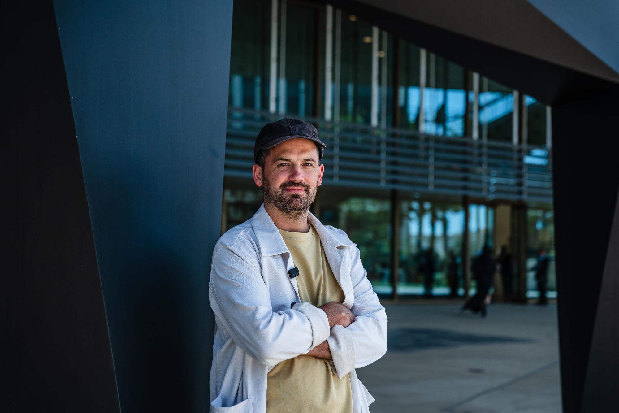 A man stands with his arms crossed in front of an art museum.