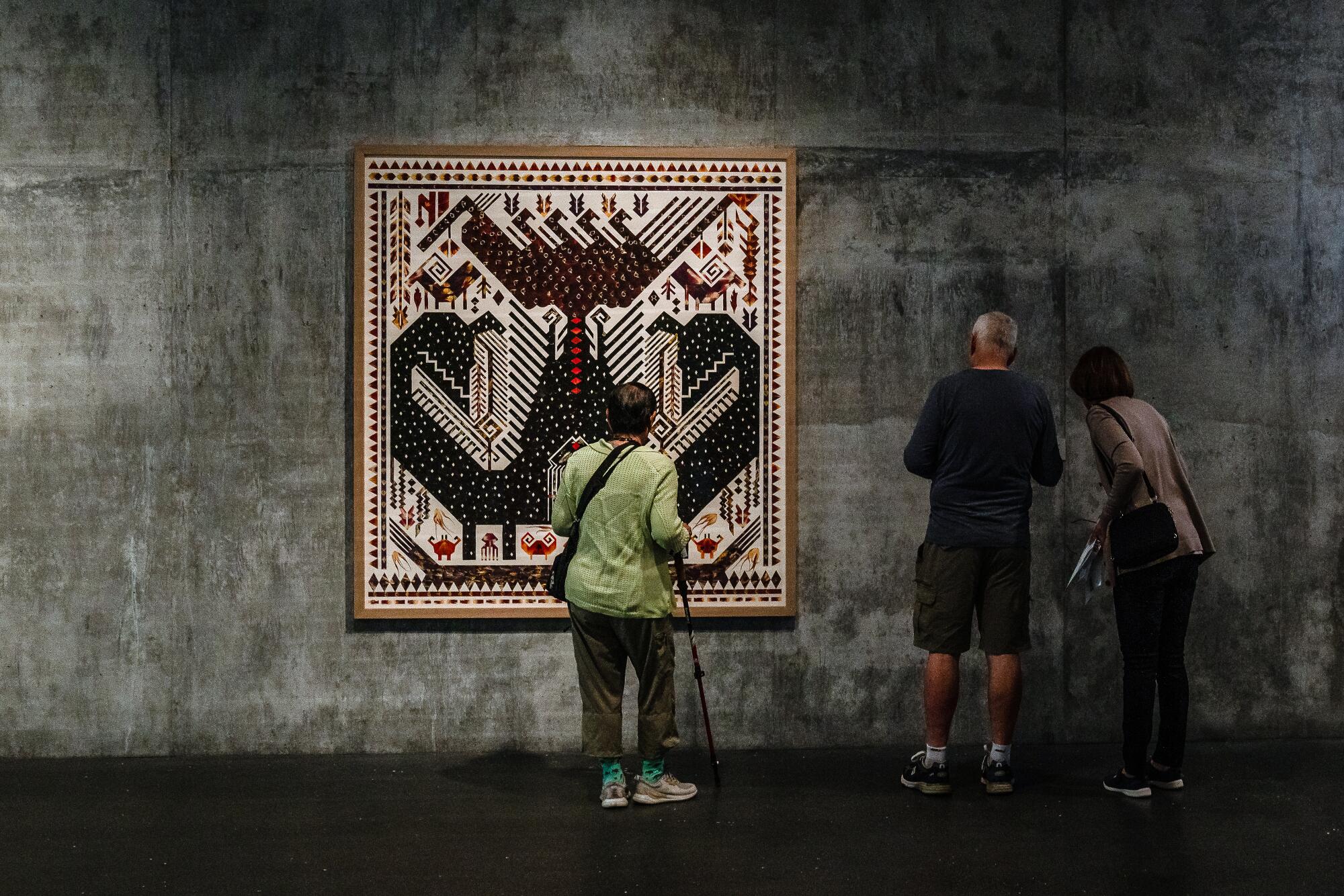 Three people are standing in front of me "Tanpan World Mountain, Ancestral Creatures, 2022" A work by Jennifer Tee on display at the museum.