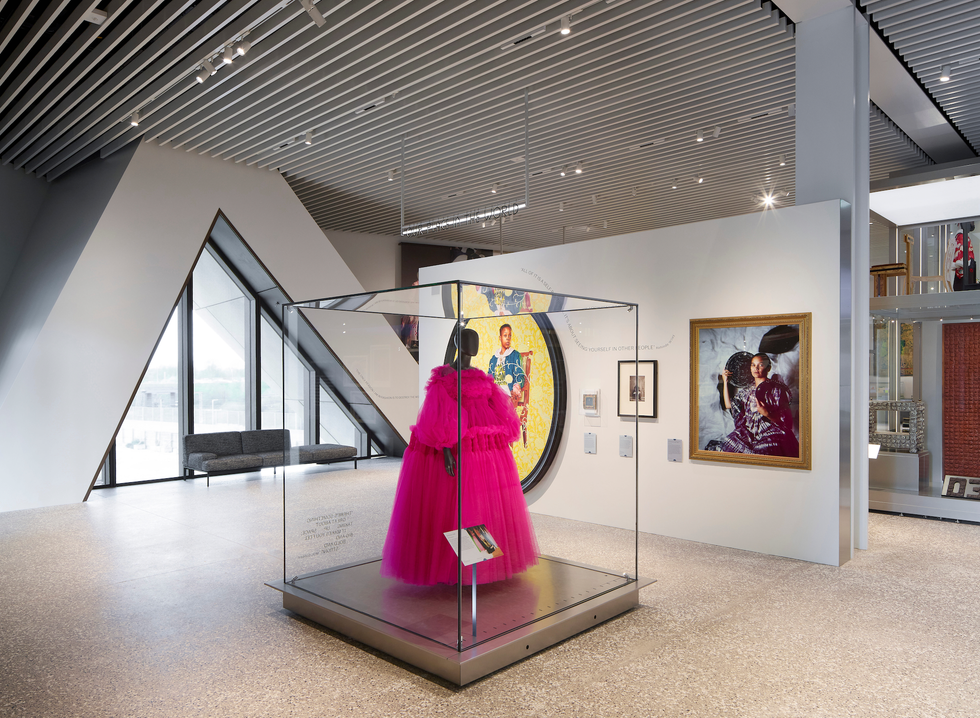 A fashion exhibit with a pink dress in a glass case.