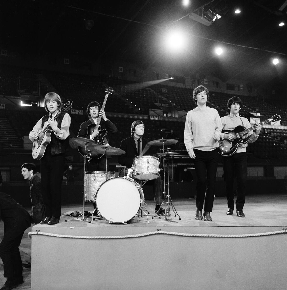 The Rolling Stones rehearse on stage under lights in 1964