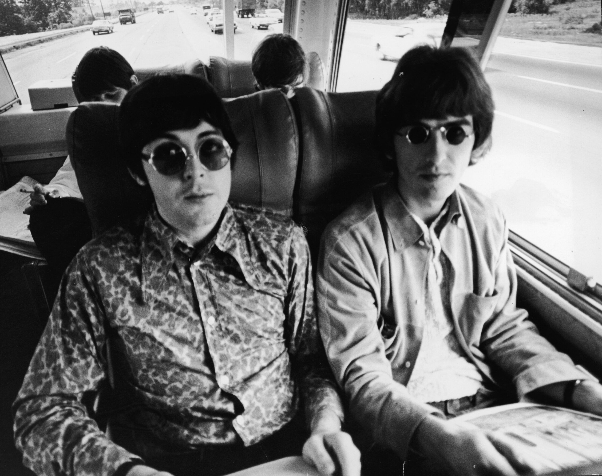 Paul McCartney (left) and George Harrison sit next to each other on the tour bus during the Beatles' American tour, c. 1966